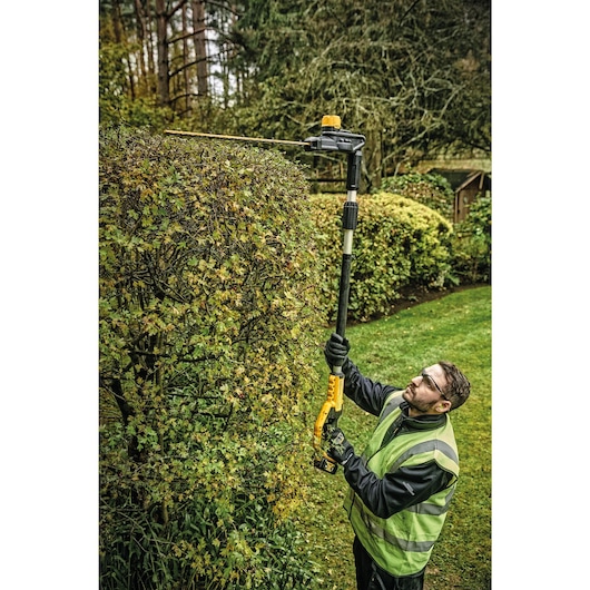 Overhead view of Pole Hedge Trimmer with battery being used by a person to cut through landscape outgrowth.