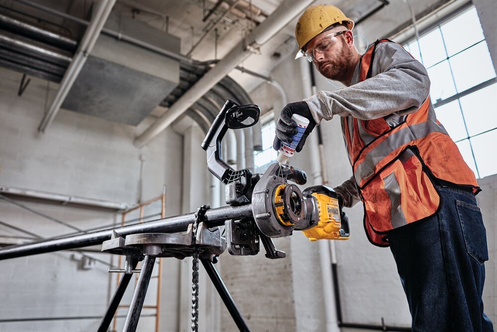 Cutting oils being applied by person to FLEXVOLT cordless pipe threader threading black iron pipe.